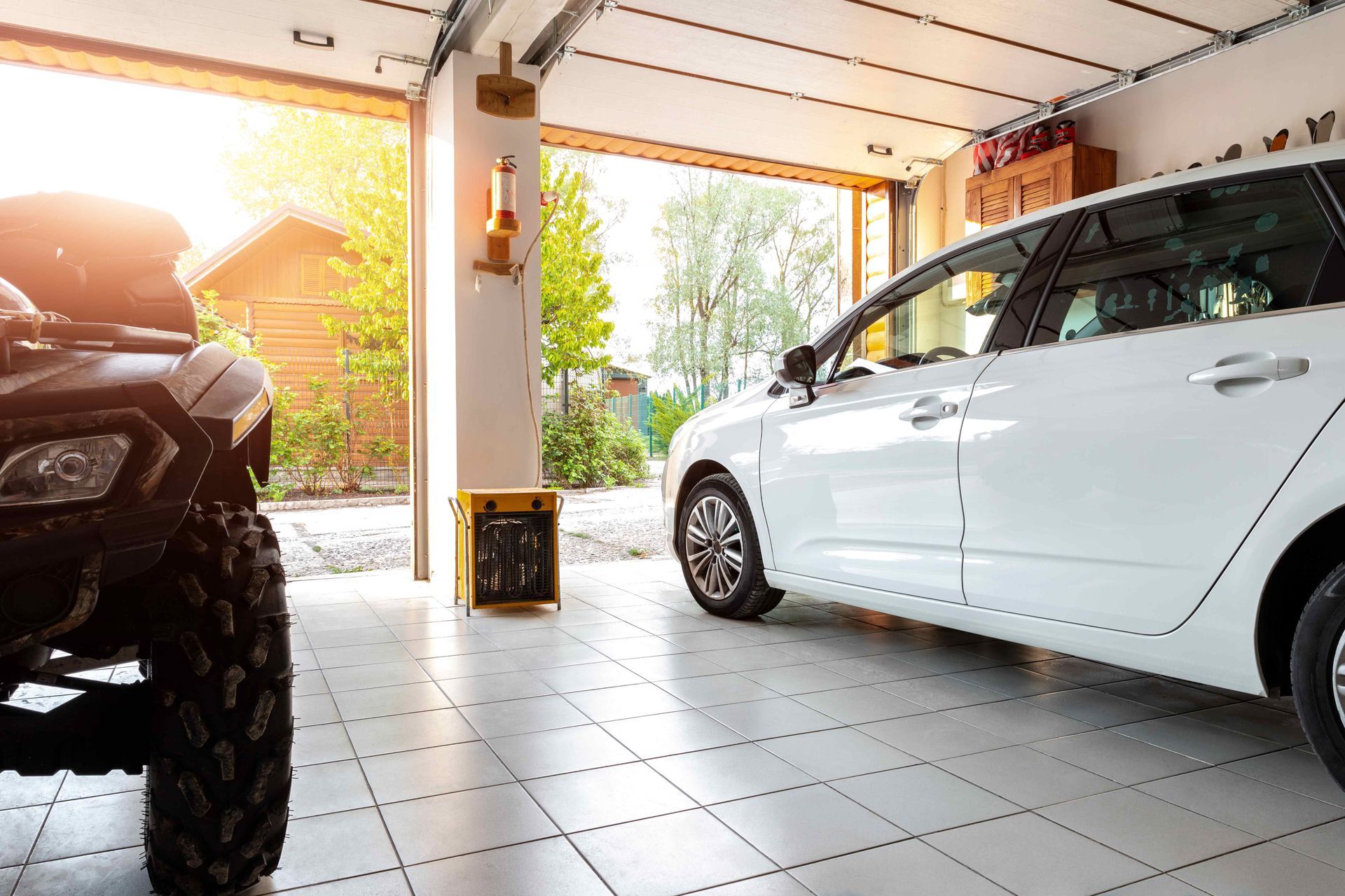 White car and ATV parked inside a sunlit open garage.
