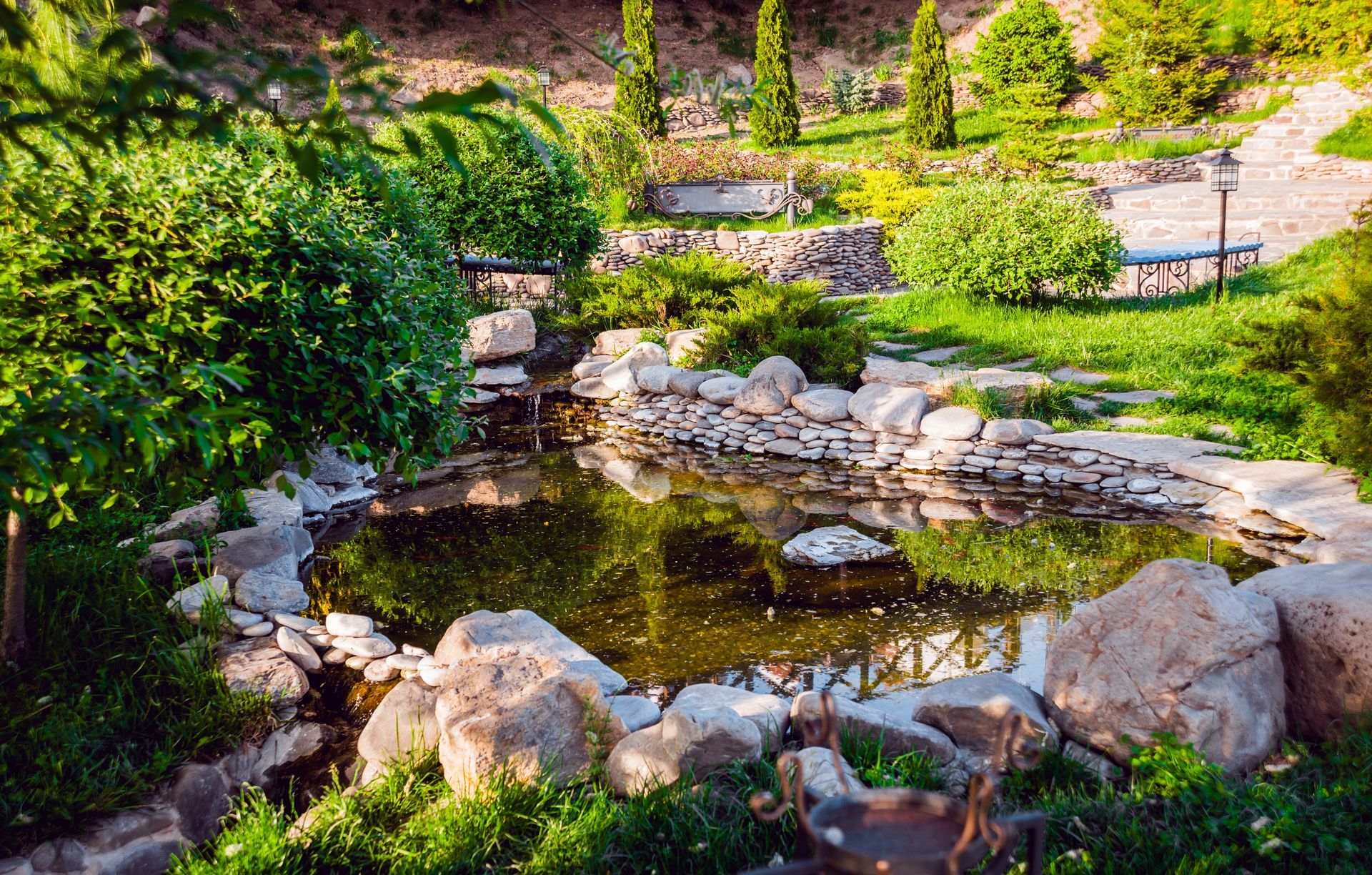 Small landscaped pond with rocks, lush greenery, and a stone path in a sunny garden Small landscaped pond with rocks, lush greenery, and a stone path in a sunny garden
