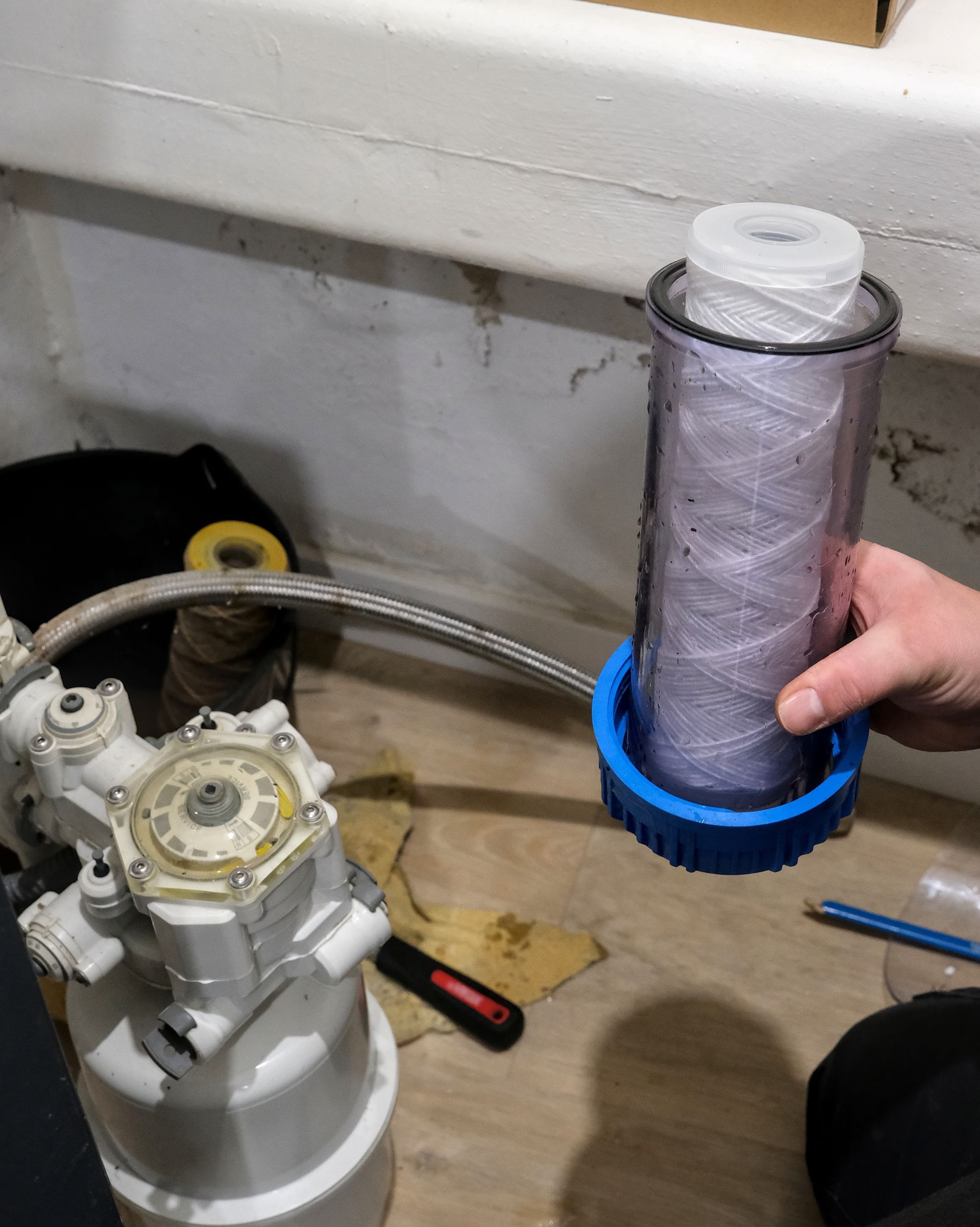 Hand holding a cylindrical filter cartridge with blue base beside a white pump on a workshop floor Hand holding a cylindrical filter cartridge with blue base beside a white pump on a workshop floor