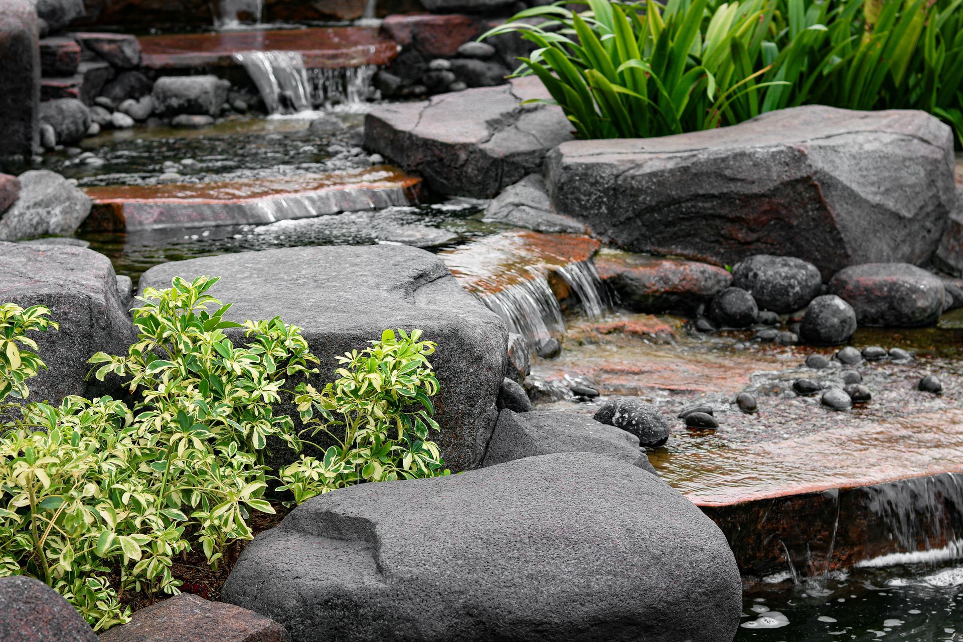 Rock garden with stacked stones, cascading water, and green plants beside a small pond Rock garden with stacked stones, cascading water, and green plants beside a small pond