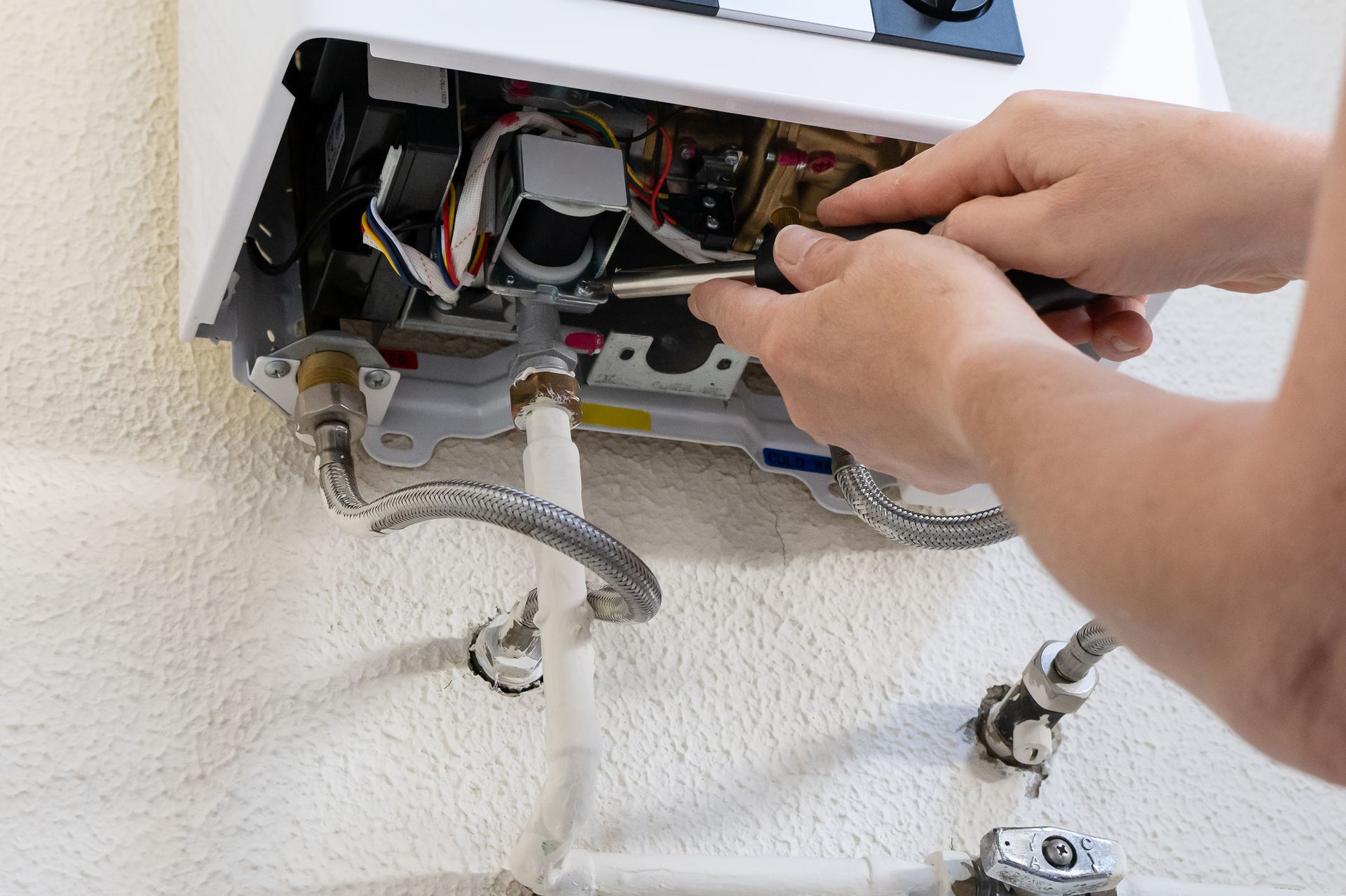 Hands repairing open electrical box with exposed wires and pipes on a wall Hands repairing open electrical box with exposed wires and pipes on a wall