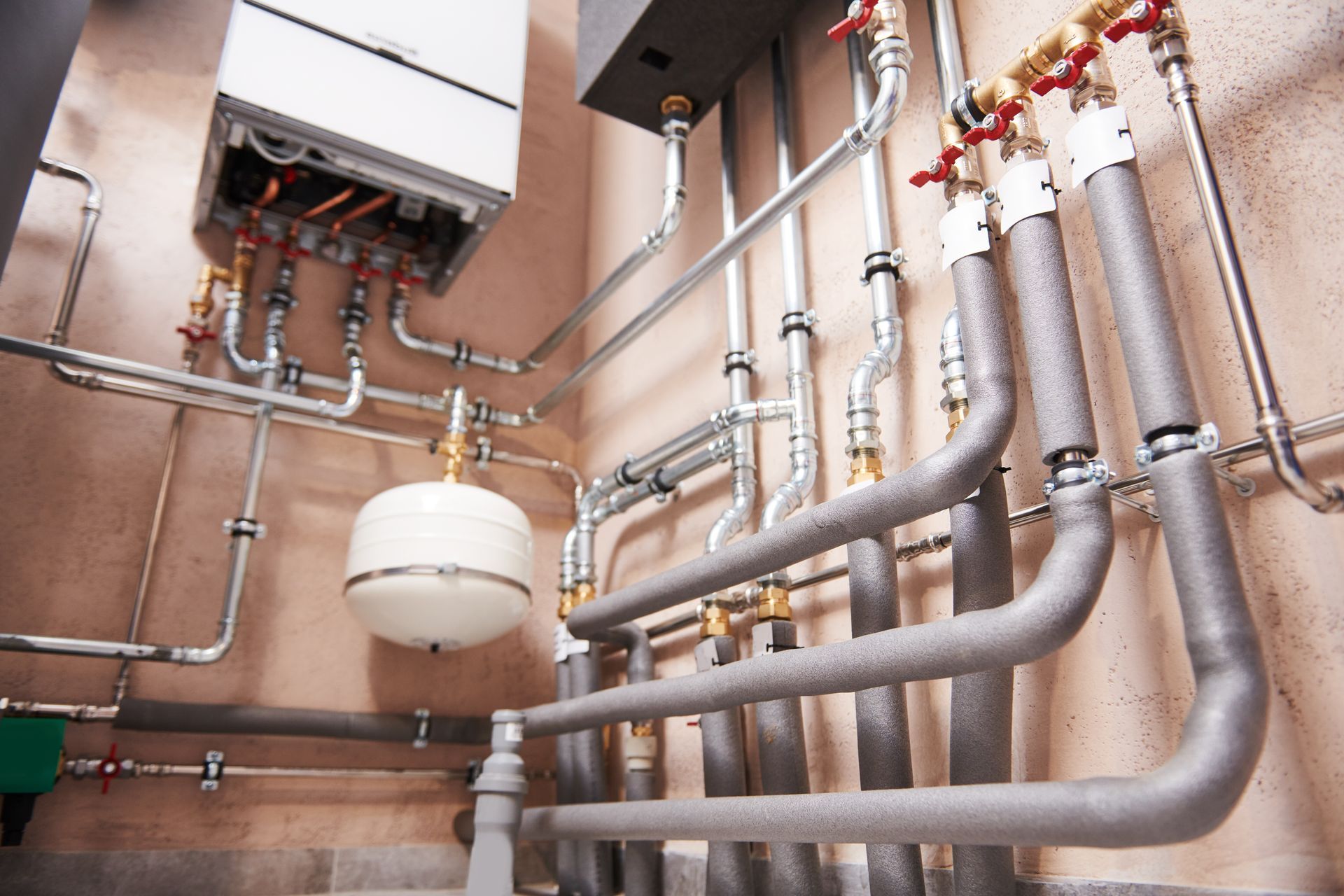 Industrial boiler room with metal pipes, valves, and a white expansion tank on a wall Industrial boiler room with metal pipes, valves, and a white expansion tank on a wall