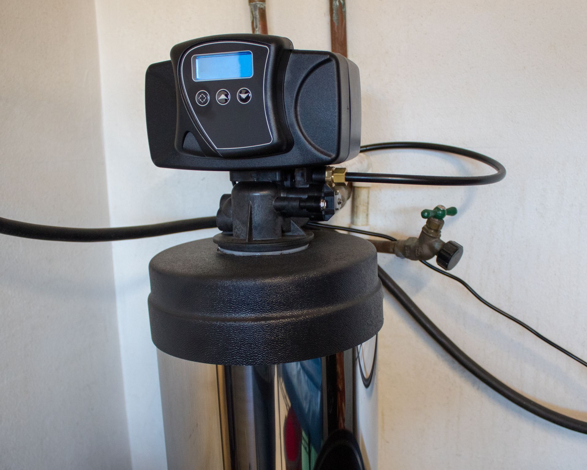 Water softener control head with digital display and hoses attached to a black tank. Water softener control head with digital display and hoses attached to a black tank.