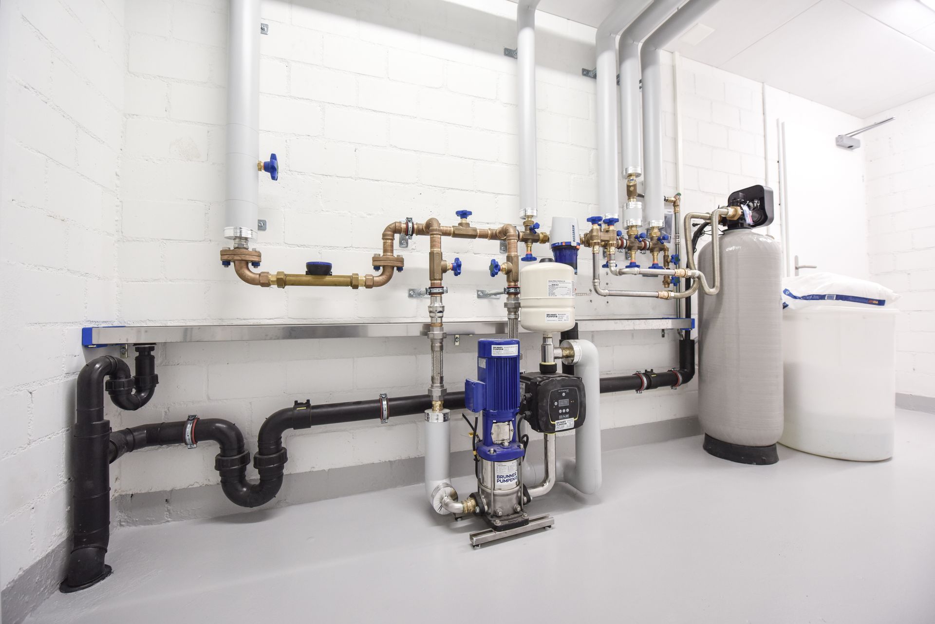 Industrial water treatment equipment with pipes, valves, pumps, and white tanks in a clean room Industrial water treatment equipment with pipes, valves, pumps, and white tanks in a clean room