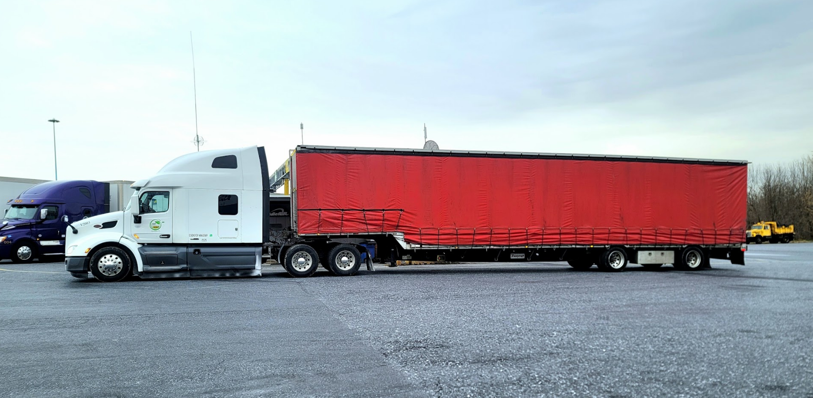 A white semi truck with a red trailer is parked in a parking lot.