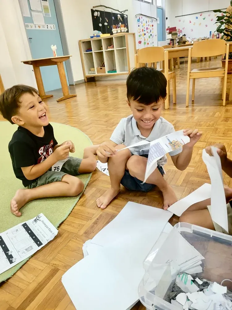 Two young boys are sitting on the floor playing with paper.
