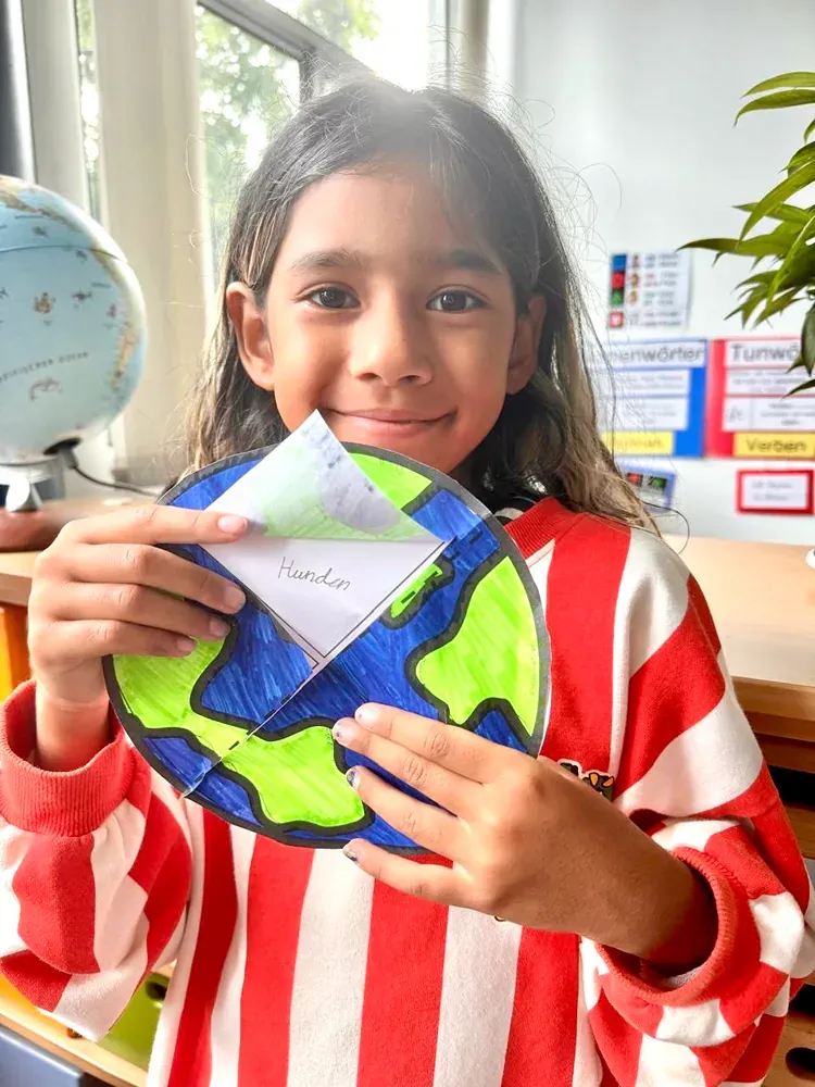A young girl is holding a paper cut out of the earth.