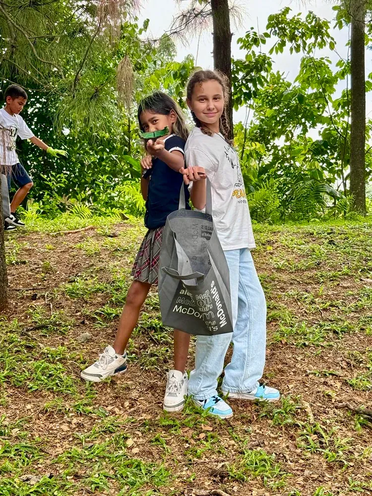 Two young girls are standing next to each other in a field holding a bag.