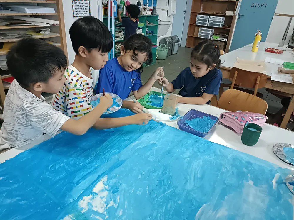 A group of children are sitting around a table painting a picture.