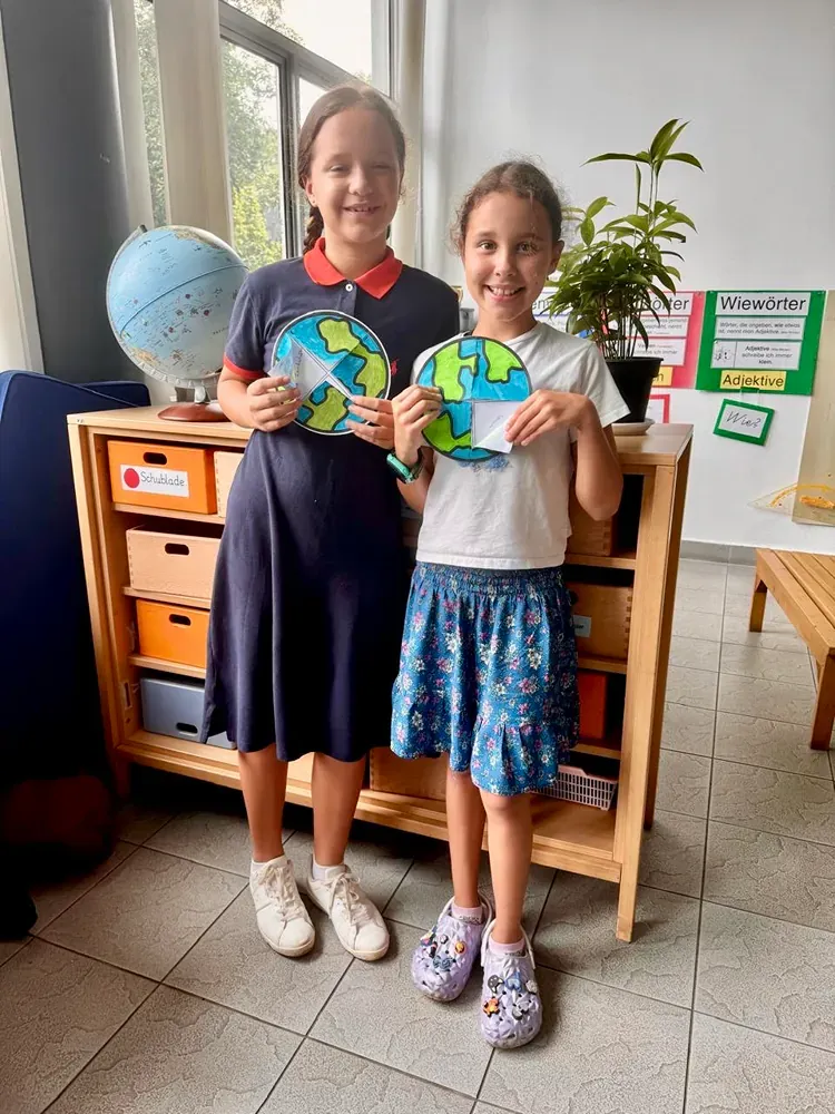 Two young girls are standing next to each other in a room holding a globe.