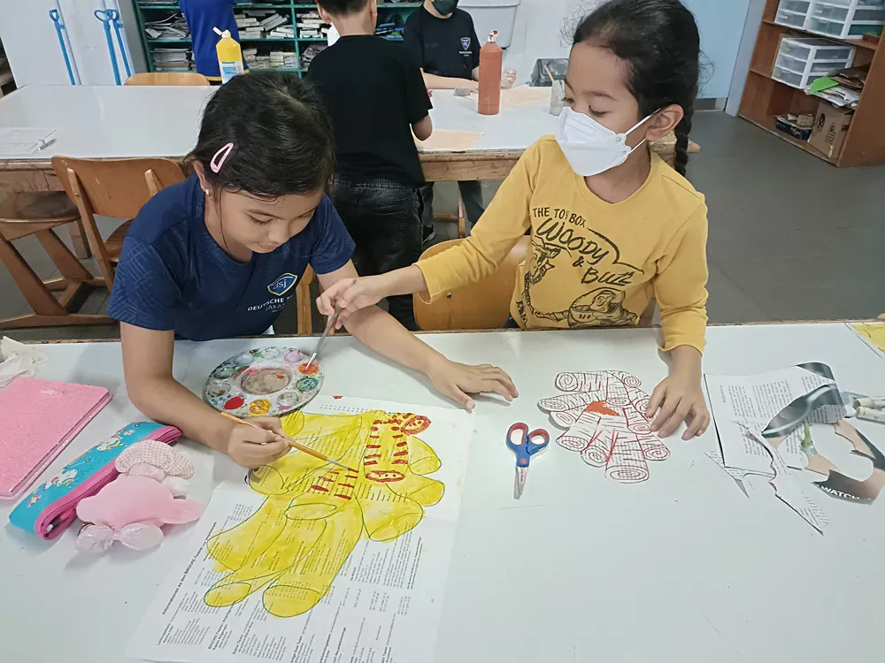 Two young girls are sitting at a table painting a picture.
