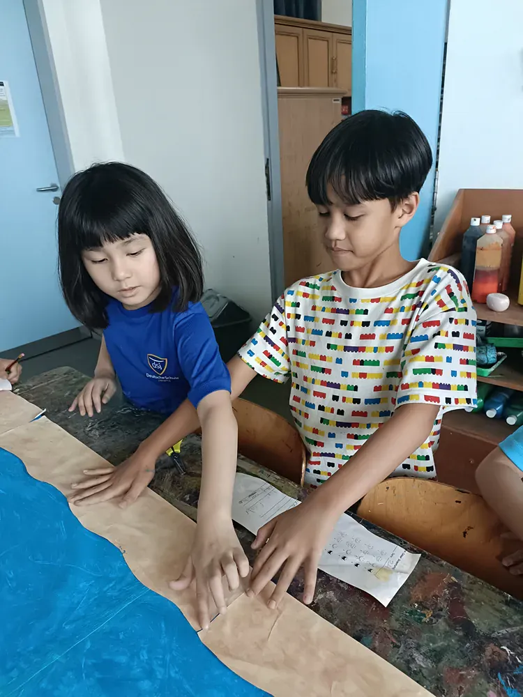 A boy and a girl are sitting at a table with their hands on a piece of paper.