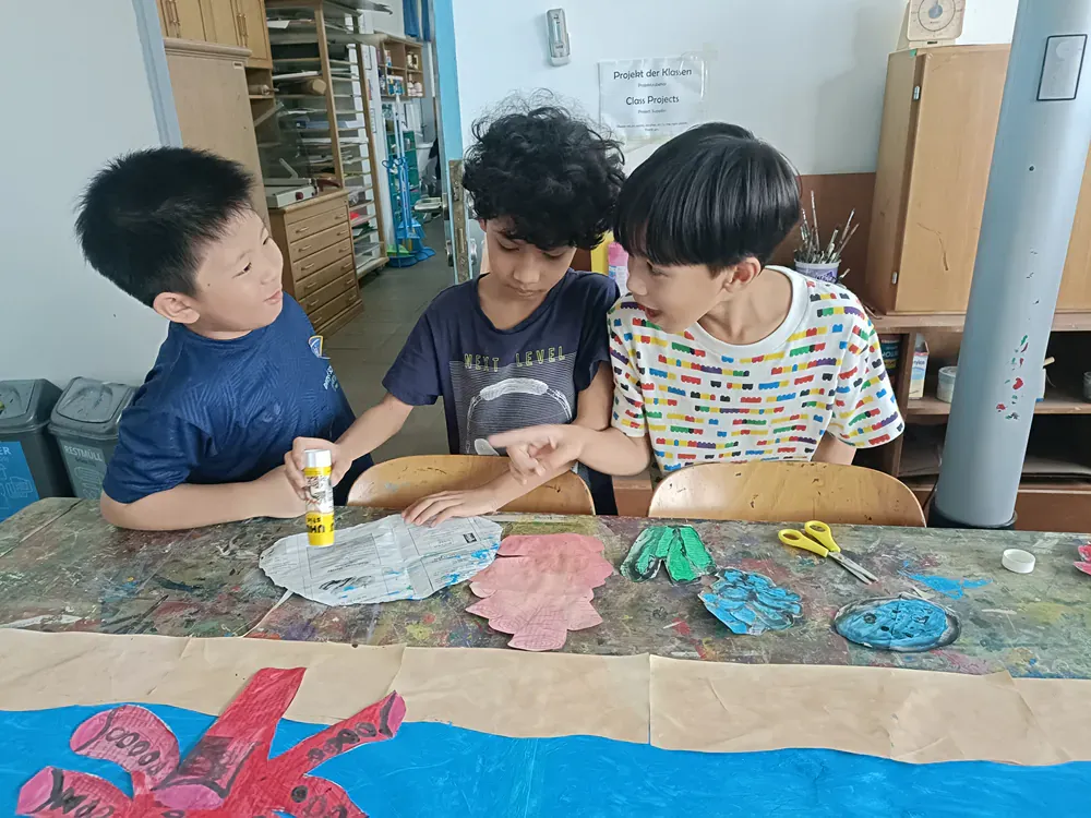 Three young boys are sitting at a table making crafts.