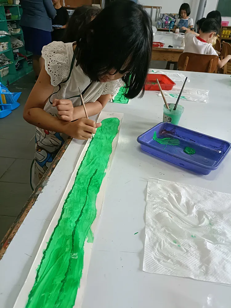 A young girl is painting a green river on a piece of paper.