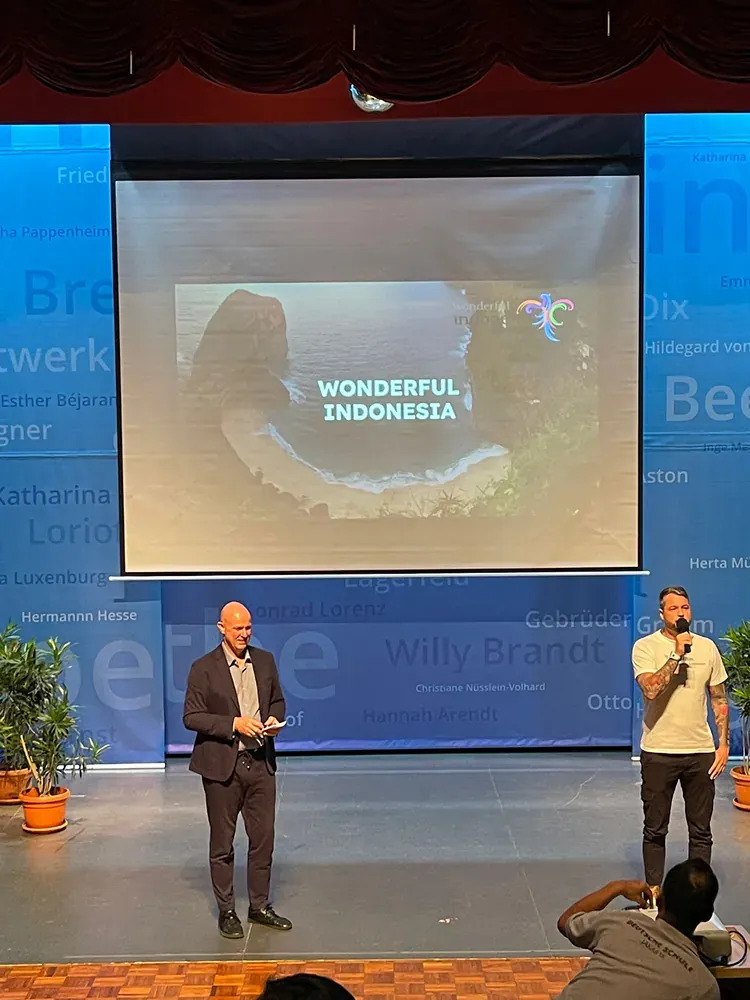 Two men are standing on a stage in front of a large screen that says wonderful indonesia.