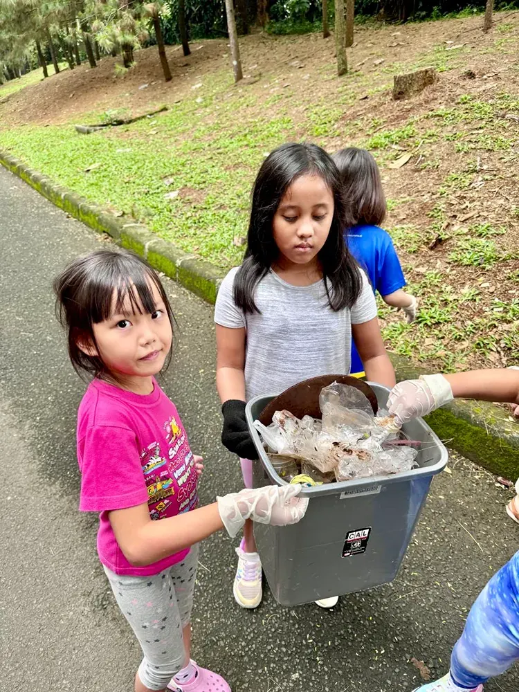 Two little girls are holding a trash can full of trash.