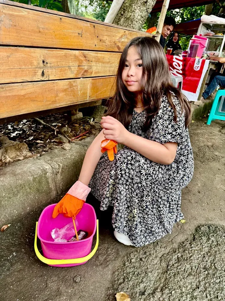 A little girl is sitting on the ground next to a pink bucket.