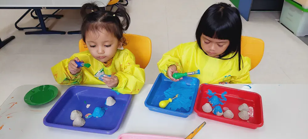 Two little girls are sitting at a table playing with clay.
