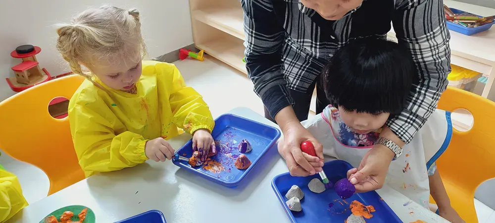 A woman is helping two children play with clay at a table.