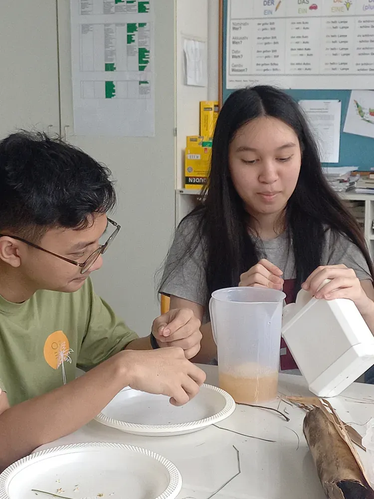 A man and a woman are sitting at a table with plates and a pitcher of liquid.