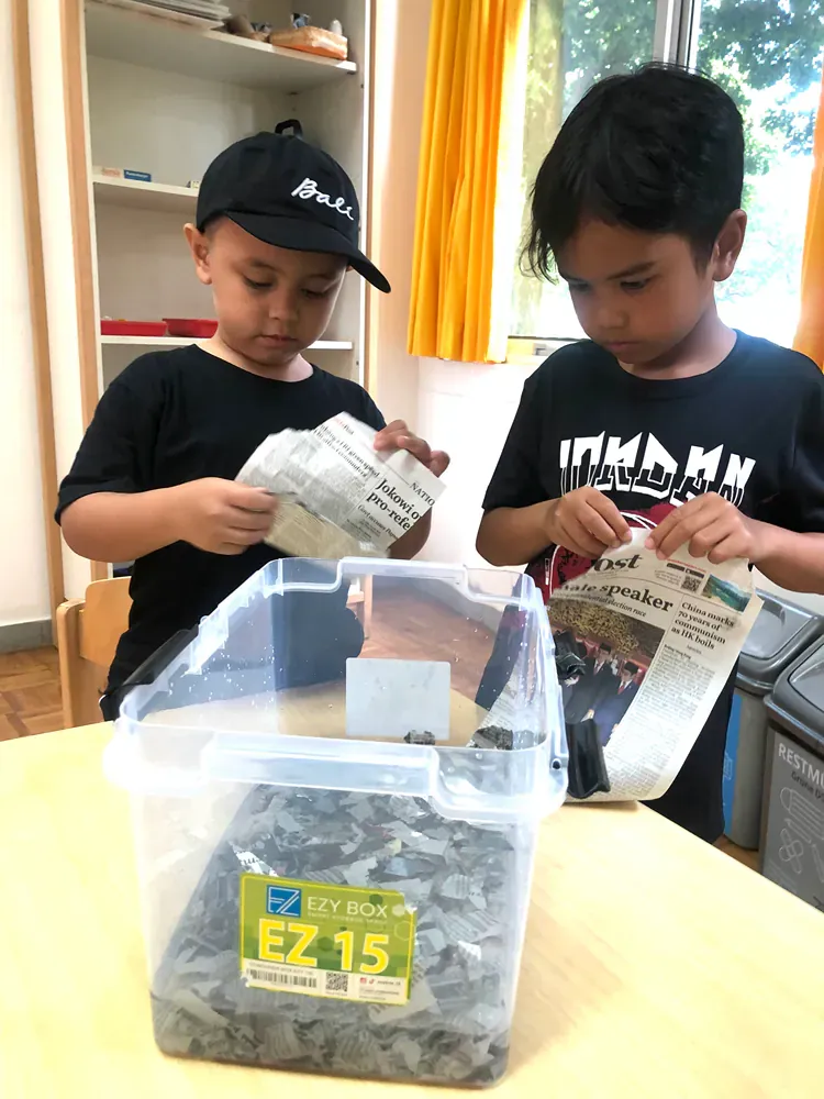 Two young boys are sitting at a table looking at a newspaper.