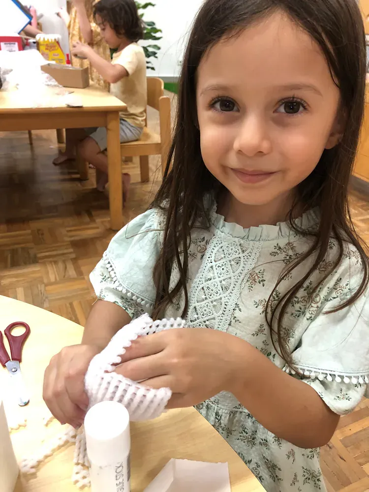 A little girl is sitting at a table holding a stick of glue