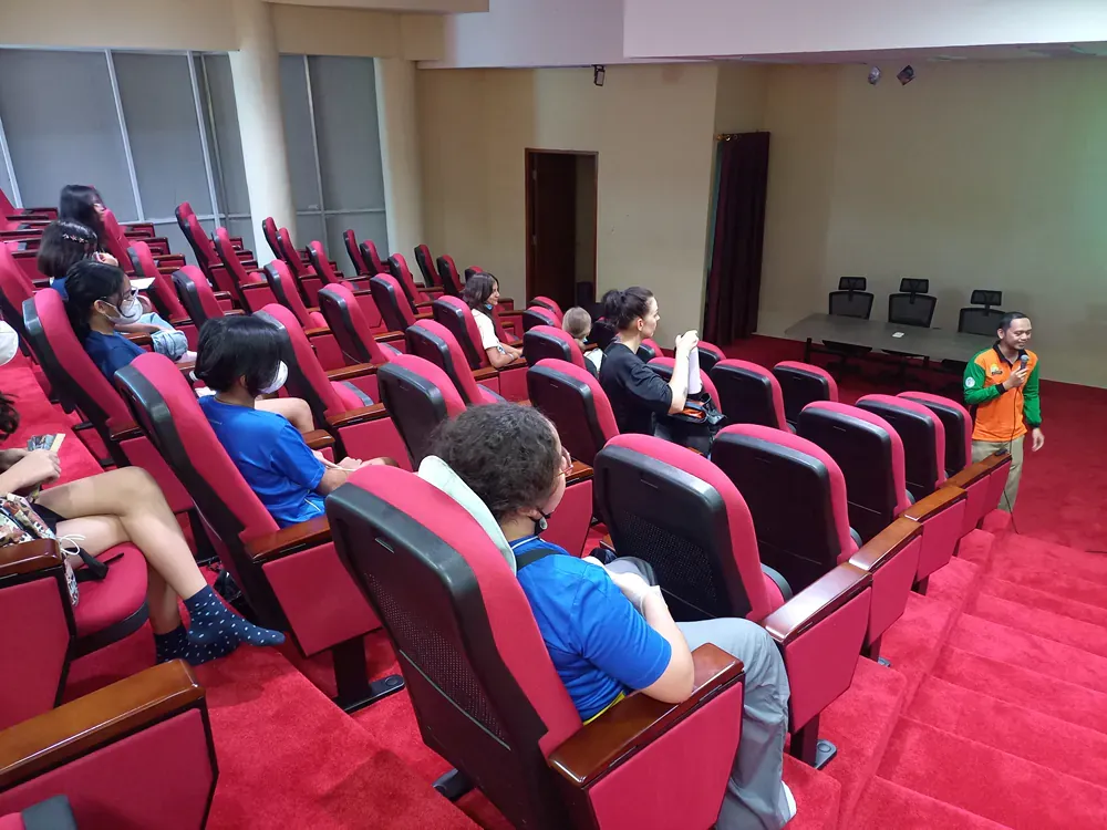 A group of people are sitting in red chairs in an auditorium.