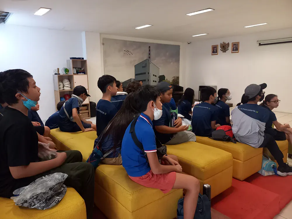 A group of people are sitting on yellow ottomans in a room.