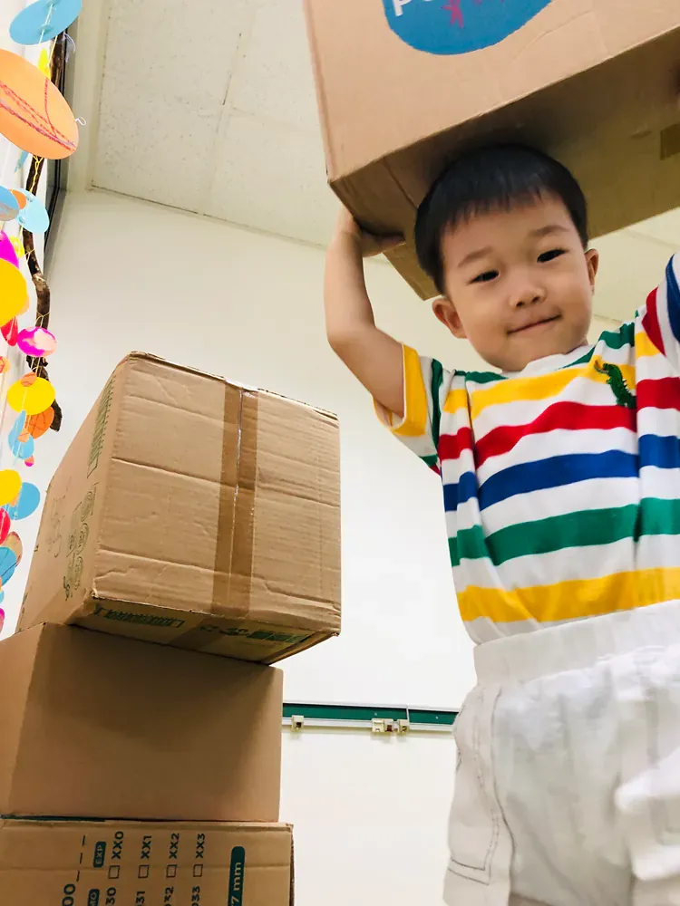 A young boy is carrying a cardboard box on his head