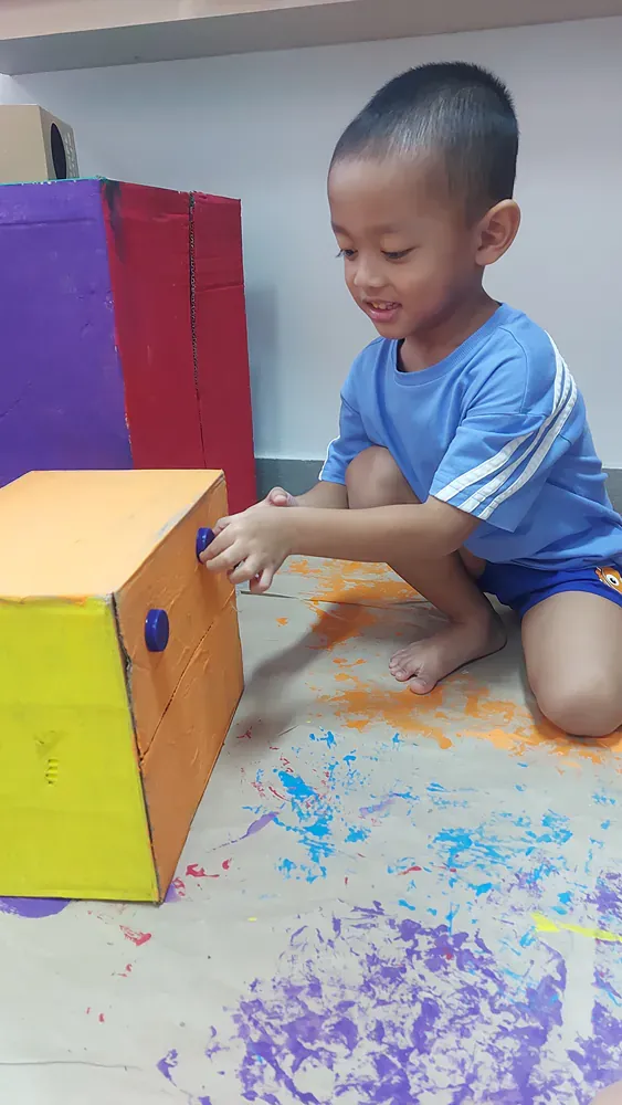 A young boy is kneeling on the floor playing with a box.