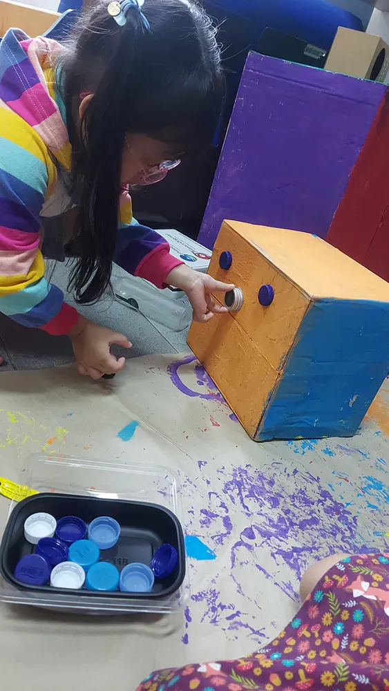 A little girl is sitting on the floor painting a wooden box.