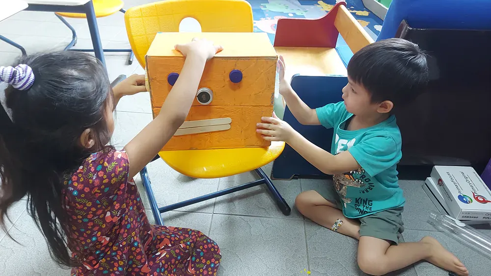 A boy and a girl are playing with a box that looks like a robot.