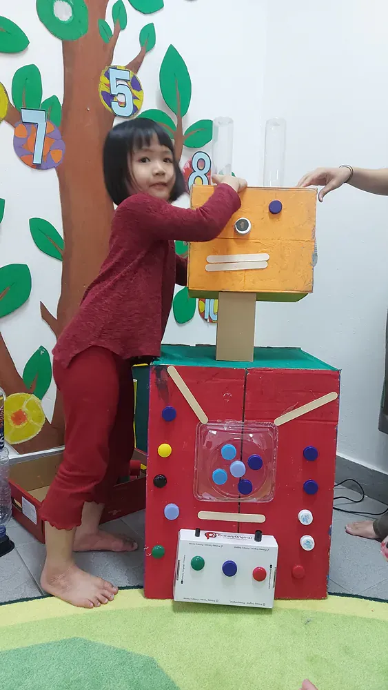 A little girl is playing with a toy robot made out of cardboard boxes.