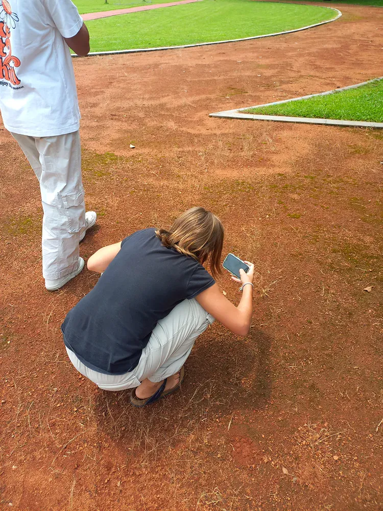 A woman is squatting down on a baseball field holding a cell phone