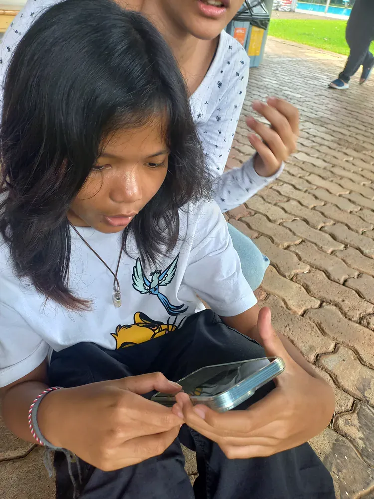 A girl is sitting on the ground looking at a cell phone.
