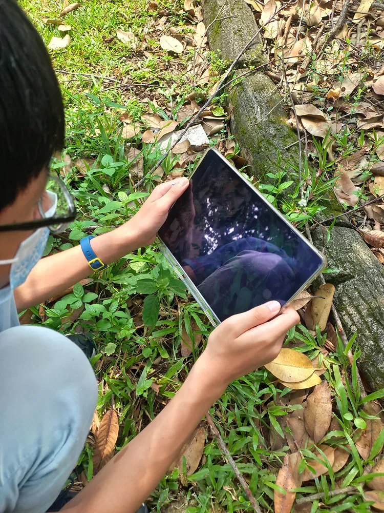 A young boy is kneeling down in the grass holding a tablet.