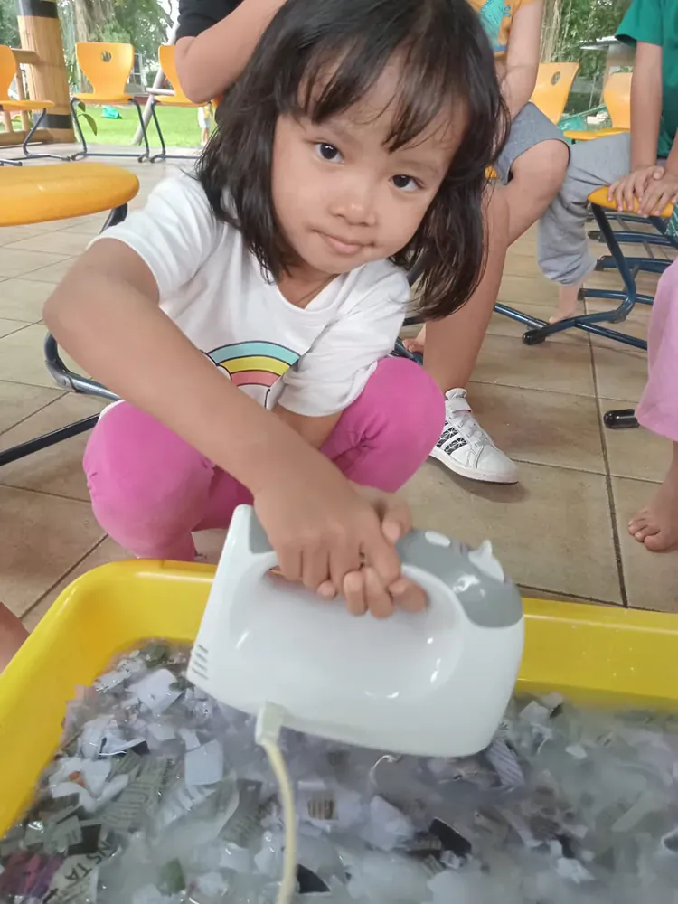 A little girl is playing with a mixer in a bowl of ice.