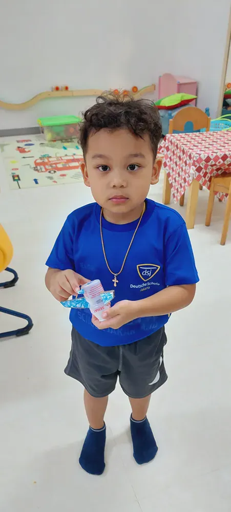 A little boy is standing in a room holding a piece of paper.