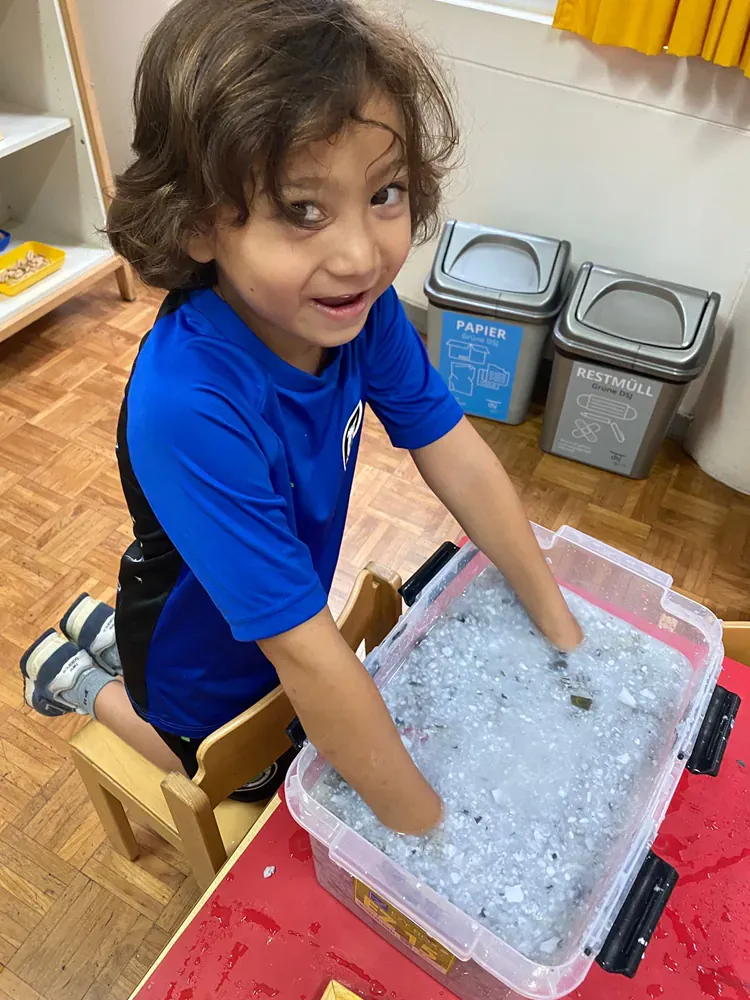 A young boy is sitting at a table playing with a plastic container filled with ice.