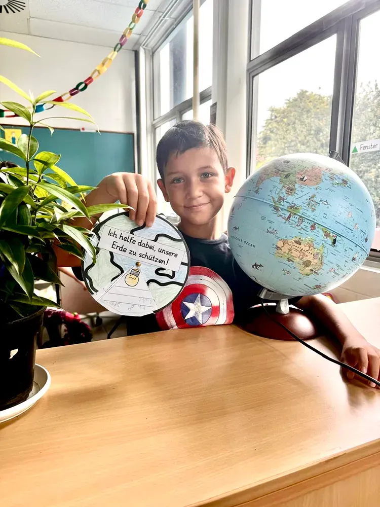A young boy is sitting at a desk holding a piece of paper and a globe.