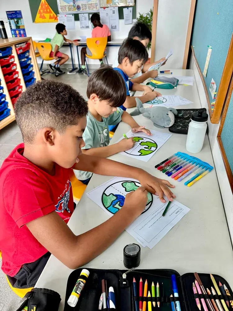 A group of children are sitting at a table drawing a picture of the earth.