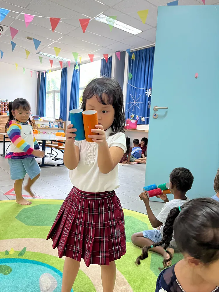 A little girl is holding a cup in a classroom.