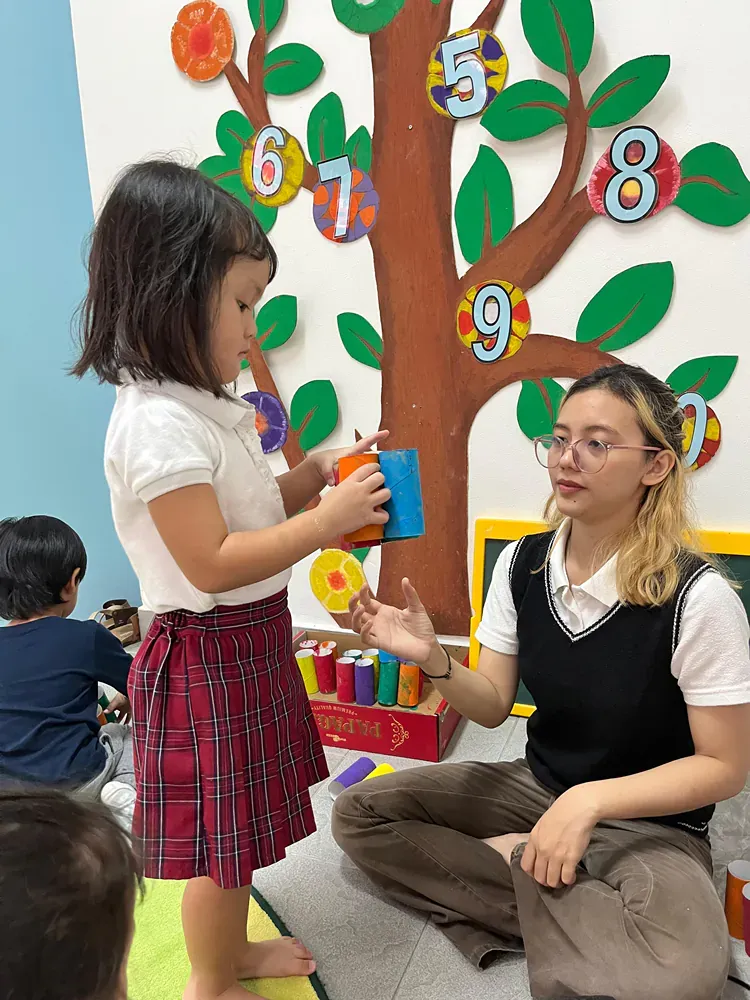 A woman is sitting on the floor talking to a little girl.
