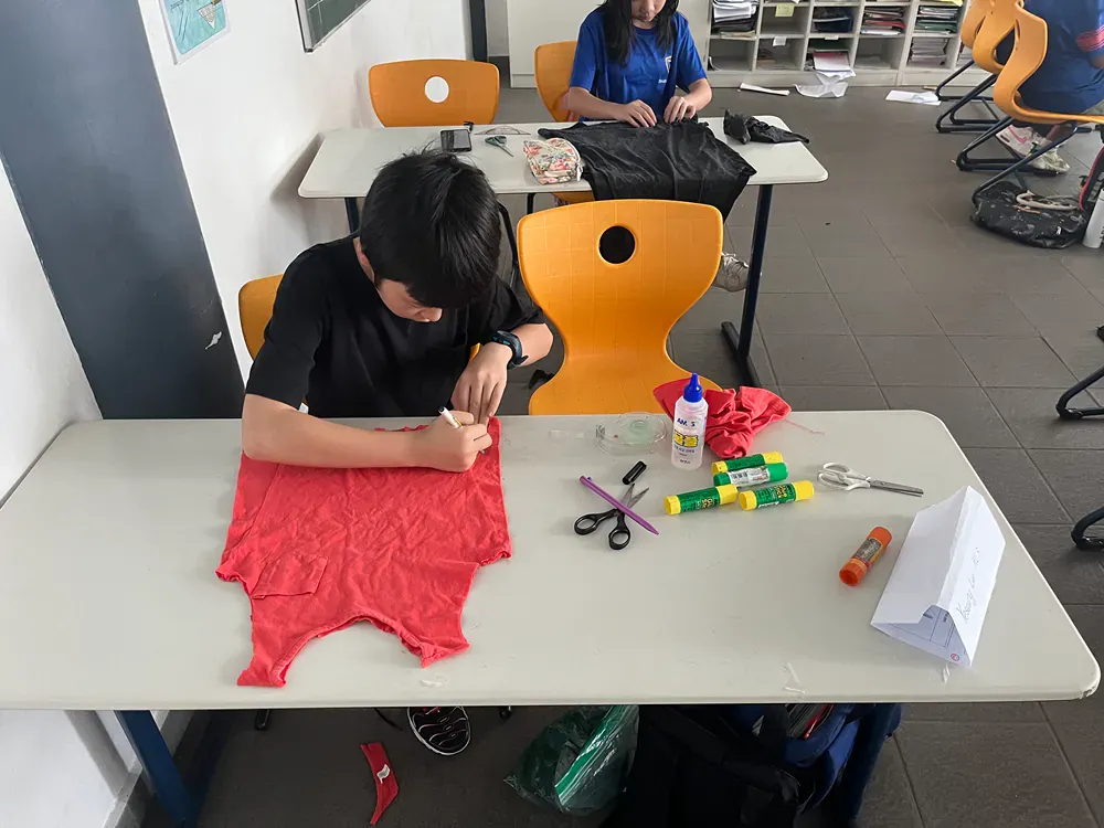 A boy is sitting at a table with a red shirt on it.