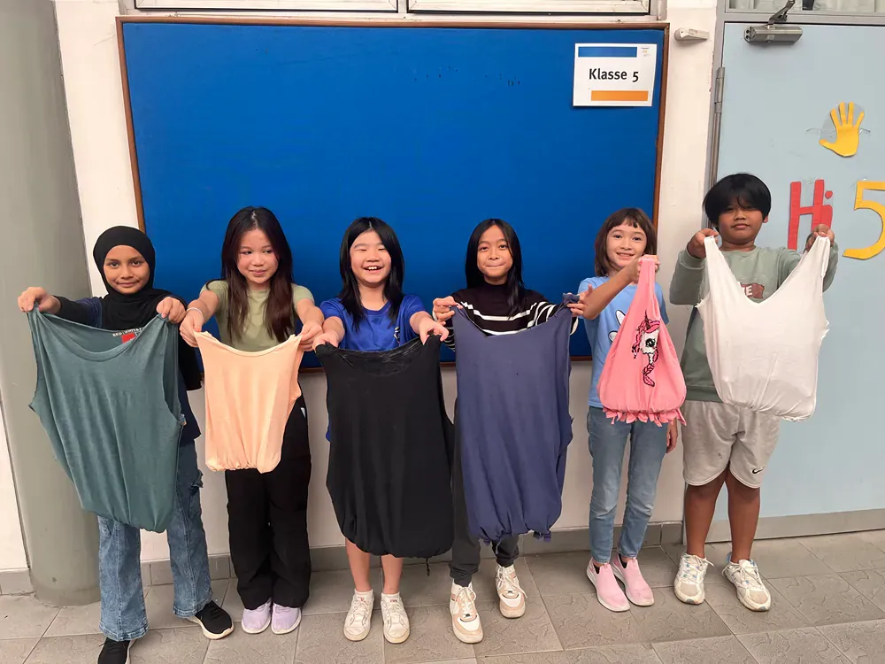 A group of children are holding clothes in front of a blue board.