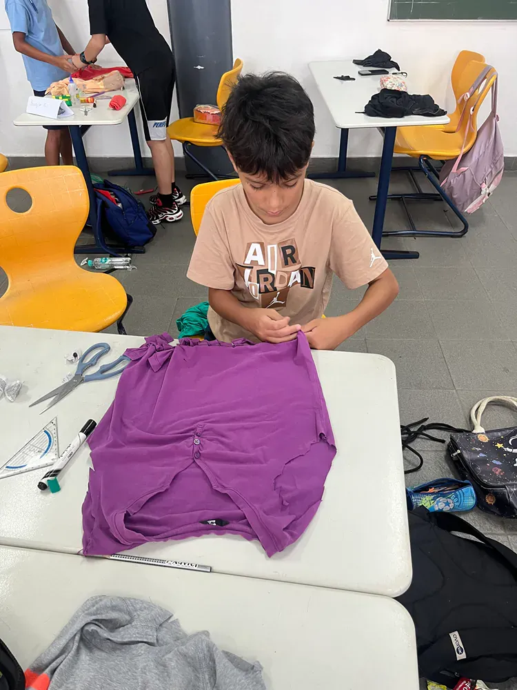 A boy is sitting at a table cutting a purple shirt