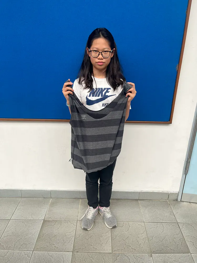 A girl is holding a striped shirt in front of a blue board.