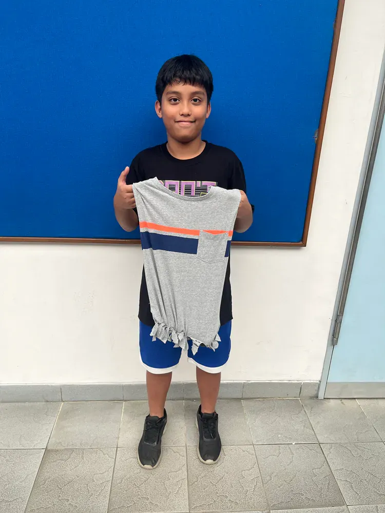 A young boy is holding a t-shirt in front of a blue wall
