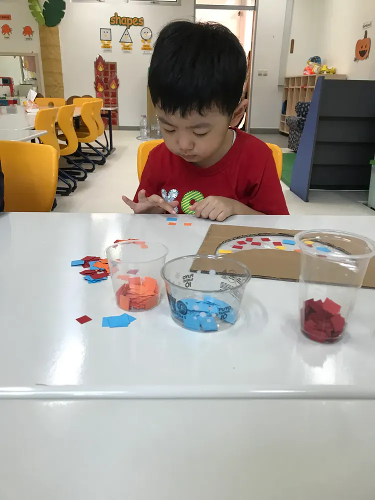 A young boy in a red shirt is sitting at a table playing with toys