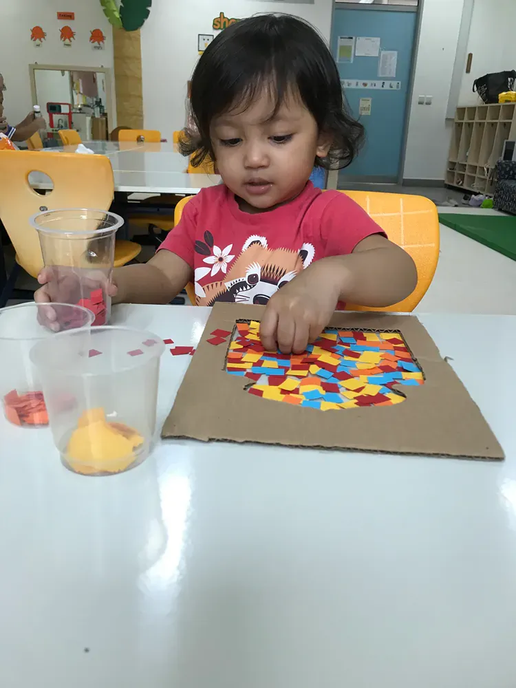 A little girl is sitting at a table playing with a piece of cardboard.